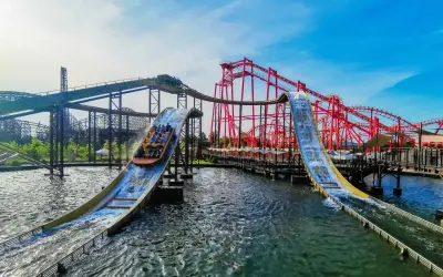Energylandia Zator atrakcje: łodzie z pasażerami zjeżdżają po stromych zjeżdżalniach wodnych, w tle czerwone rollercoastery.