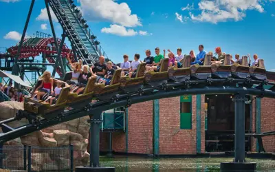 Energylandia Zator atrakcje: wagonik kolejki górskiej z pasażerami pędzi nad wodą, w tle widać konstrukcję kolejki i budynki parku.
