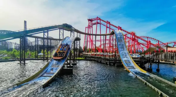 Energylandia Zator atrakcje: łodzie z pasażerami zjeżdżają po stromych zjeżdżalniach wodnych, w tle czerwone rollercoastery.