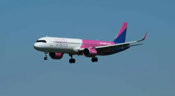 Samolot Wizz Air z różowym i niebieskim ogonem leci na tle błękitnego nieba.