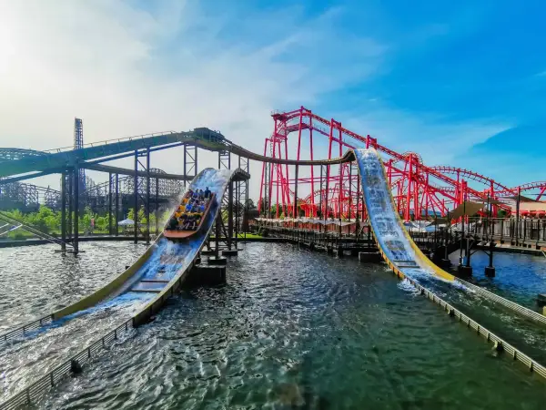 Energylandia Zator atrakcje: łodzie z pasażerami zjeżdżają po stromych zjeżdżalniach wodnych, w tle czerwone rollercoastery.