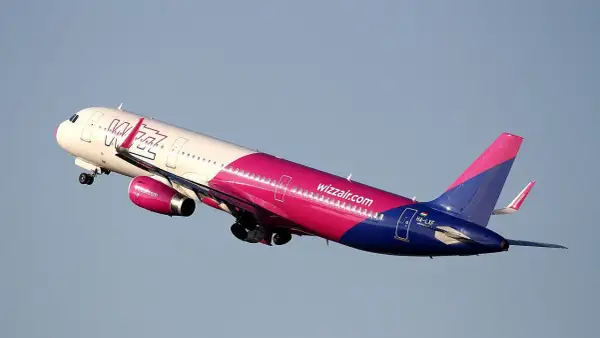 Samolot Wizz Air w różowo-niebieskich barwach wznosi się na tle błękitnego nieba.